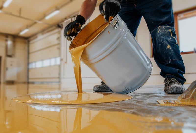 Installer pouring amber epoxy resin from a bucket onto prepared concrete
