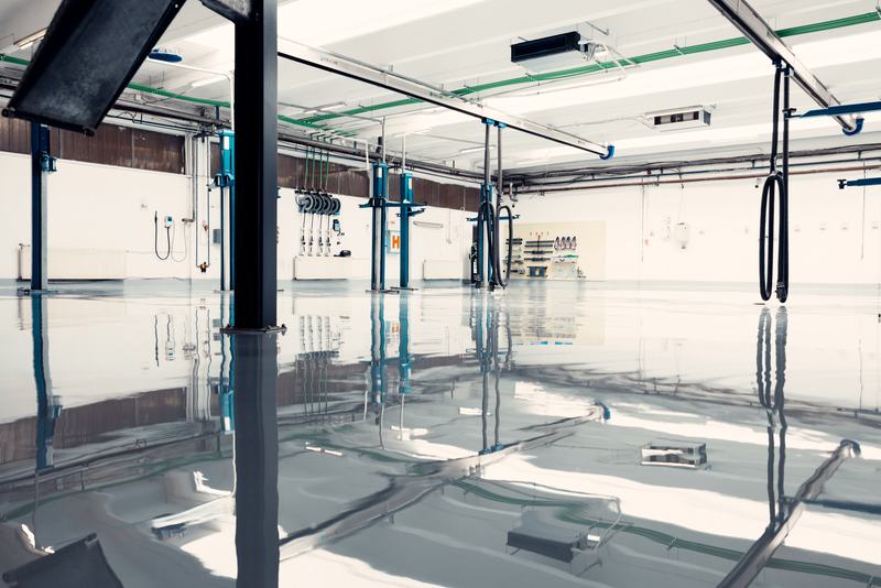 Light gray high-gloss epoxy floor reflecting blue vehicle lifts in a clean auto service bay